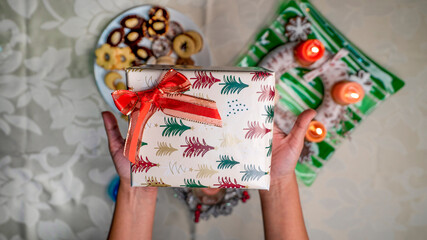Fototapeta premium Christmas present in hands with christmas decoration and traditional sweets on the table.