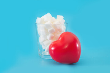 Heart near glass full of white sugar, studio shot of sweet food ingredient isolated on blue background,