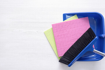 Broom, dustpan and rag on the white wooden floor background with copy space.