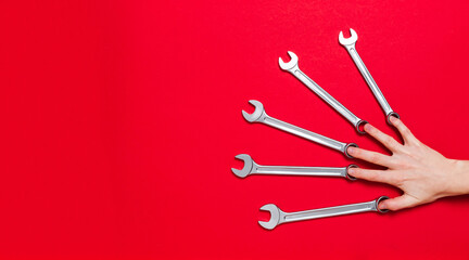 Hand fingers hold a set of wrenches different size on a red background. Banner with tools and copy space with industrial holiday concept. Business card or certificate of auto service. Instrument shop