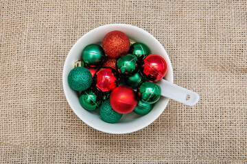 Red and green Christmas baubles in white bowl with spoon. Creative Christmas background