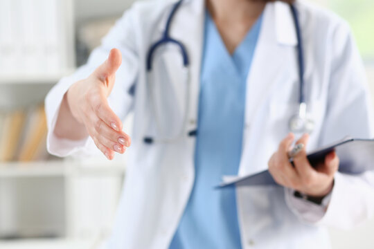 Female medicine doctor hold pad and give arm to shake in office closeup. Friend welcome, introduction or thanks gesture, test work, examine patient, congratulation, help exam, teamwork deal concept