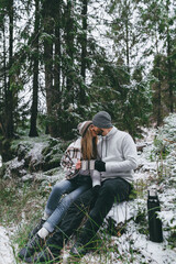 Kissing couple with mugs of hot drink in snowy forest