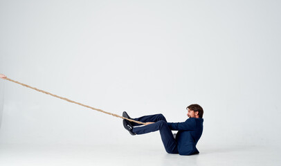 a business man lies on the floor and pulls a rope on a light background indoors