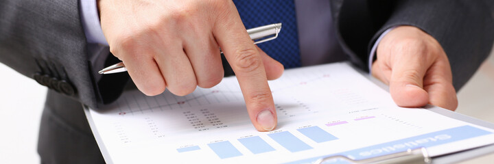 Hand of businessman in suit filling and signing with silver pen partnership agreement form clipped to pad closeup. Management training course, some important document, team leader ambition concept