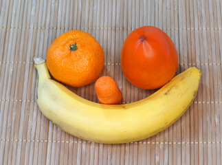 Berry and vegetable smile. Persimmon, tangerine, peeled carrots and banana on a bamboo napkin - a set of juicy and fresh sweet fruits to the table.
