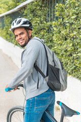 Fototapeta na wymiar Young black man sitting on a bike in a park, leaning on the handlebars smiling, side view