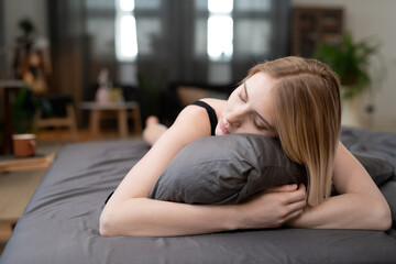 Young serene blond woman in black lingerie embracing pillow while sleeping