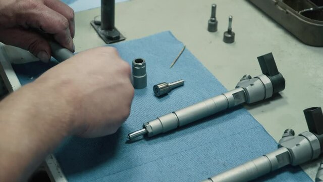 Diagnostics and repair of car nozzles. The mechanic tears apart the nozzle on the table. Close-up of hands.