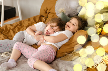 Two cute girls are playing all over the bed. Two sisters in a New Year's interior