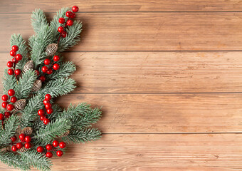 Christmas fir branches with decorative red berries are on a wooden background. Free space for text.