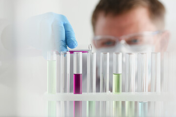 A male chemist holds test tube of glass in his hand overflows a liquid solution of potassium...