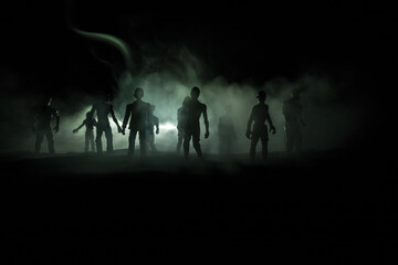 Fototapeta premium Scary view of zombies at cemetery dead tree, moon, church and spooky cloudy sky with fog, Horror Halloween concept with glowing pumpkin. Selective focus