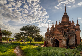 Fototapeta na wymiar Ancient Buddhist pagoda against cloudy sky in the old city of Bagan, the world heritage site in Myanmar (Burma). Carriages with tourists in the background.