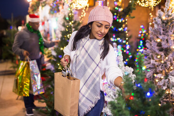 Positive woman choosing New Year's tree in christmas street fair