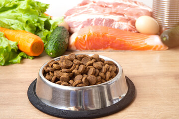 Dry pet dog food with natural ingredients. Raw meat, fish, vegetables, eggs and salad near bowl with dry pet feed. concept of a correct balanced and healthy nutrition for pet