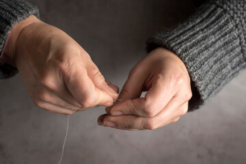 Closeup of female hands threading a needle on gray background