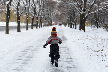 Fototapeta na wymiar Boy runs through the park in winter. Back view. Child walks in snowy park.