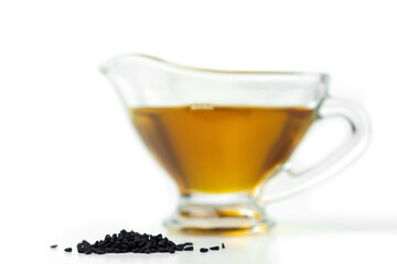 A handful of black cumin seeds on the background of a glass gravy boat with black seed oil. Selective focus. On white.