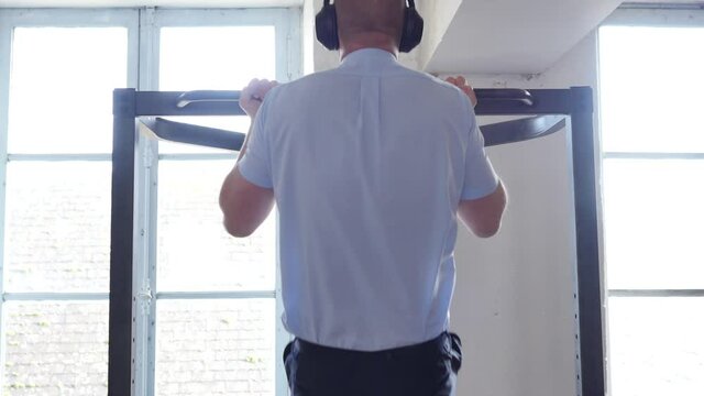 Rear view of company worker in suit doing pull ups. Handsome caucasian man in suit with shirt doing pull ups at the gym. pull up exercise on horizontal bar in gym. Sports, fitness, gymnastics workout.