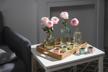 Rose White Pink O'hara. Pink roses in three different shaped bottles on a tray with five small espresso cups on the coffee table