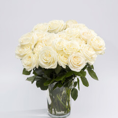 A bouquet of white Roses Playa blanca is in the glass vase on the grey background.