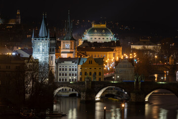 .old stone charles bridge and bridge tower on vltava river and light from street light in and roofs of surrounding buildings of prague city center at night