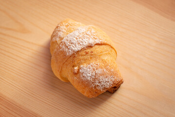 Tasty croissant seasoned with sugar on wooden table. Cooking biscuits