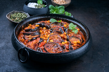Modern style slow cooked Lebanese vegetarian eggplant stew maghmour served with chickpeas and yoghurt as close-up in a design pot