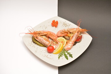 Large shrimps on a white plate. Decorated with lemon wedges. Located on a black and white background. Can be used in the restaurant menu.