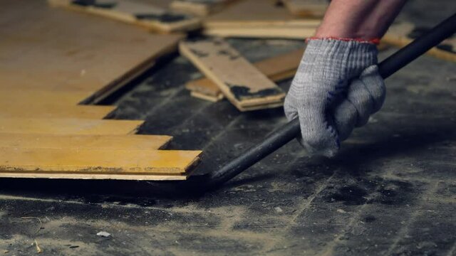 Worker removes old parquet using a tire iron tool during a flat renovation. Demolition of old wooden parquet. 4K resolution video.