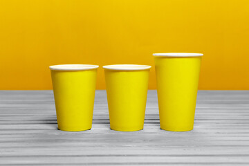 Mockup of three yellow paper cups. Disposable coffee cup in trending color.