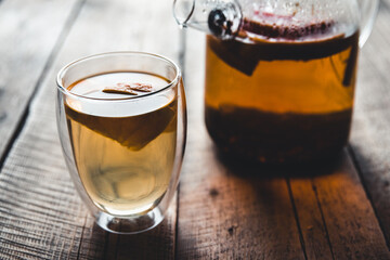 Citrus tea in a transparent teapot and a glass, healthy drink on a wooden background.