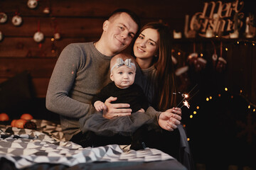 cute young family dad, mom and baby girl with sparklers on bed with Christmas background behind.