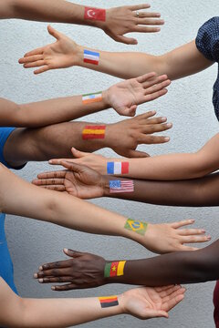 International brothers and sisters, men and woman from different nations with flags painted on their arms stretching out their hands to each other in peace