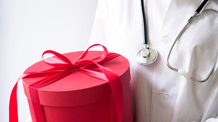Concept for christmas and new year medical banner.Female doctor in white coat,stethoscope,latex gloves holds big red gift box with bow.Gift for birthday,doctor's day,March 8,mother's day.Copy space