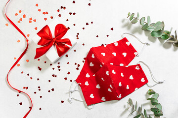Fototapeta premium St. Valentine’s Day in pandemic time concept. Gift box, shining decorations and red protective masks on white marble background. Lockdown and holidays concept.
