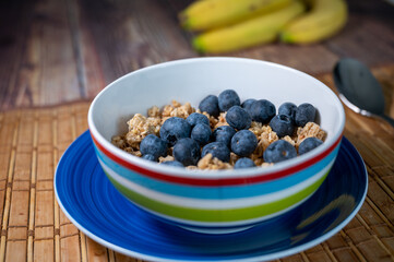 Colourful bowl of cereal and blueberries with bananas in the background