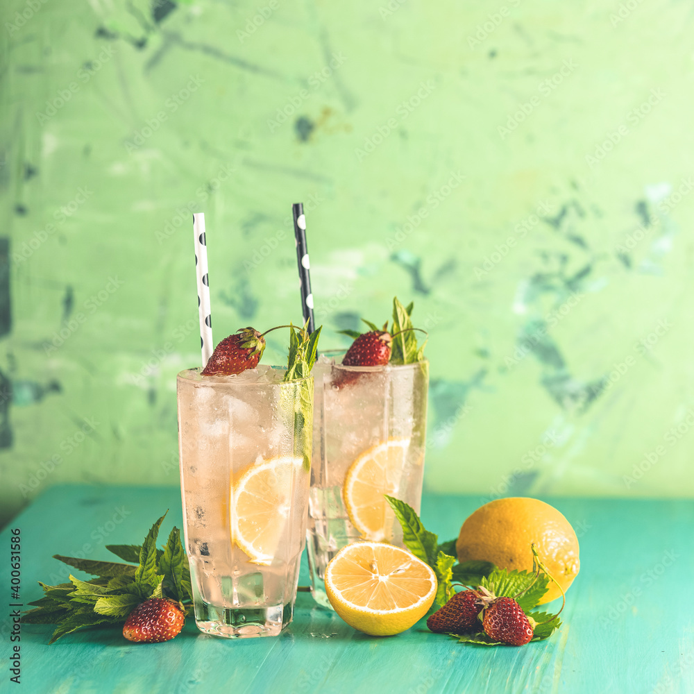 Wall mural two glasses of cold icy refreshing drink with lemon and strawberry served with bar tools on green wo