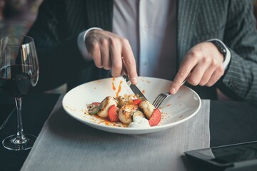 A young attractive man eating cottage cheese pancakes with sour cream and almond flakes and sea buckthorn-orange sauce in an indoor restaurant