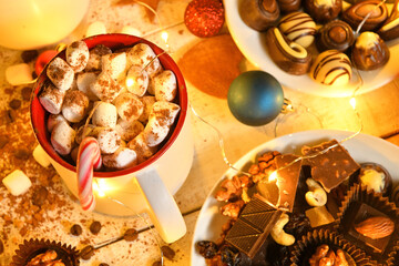 sweet food top view background for merry christmas or new year holiday decoration with night illumination - chocolate candies, tangerines, cookies, marshmallow and cocoa latte on white wood
