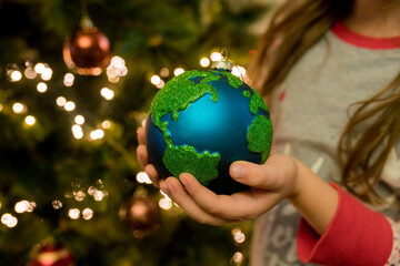 Close-up of little girl hanging Xmas glass bauble decoration ornament globe planet earth on...