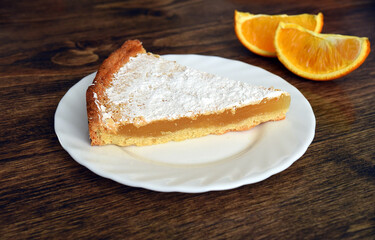 Piece of homemade pie with lemon and orange filling, covered with powdered sugar on a wooden table near orange fruit