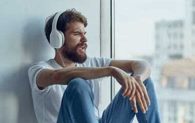 a man in headphones sits on the windowsill and listens to music imitation driving a car steering wheel Studio