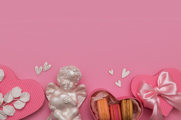 Valentine's day flat lay with gift box, macaroon, bow, angel, hearts on a pink background with copy space