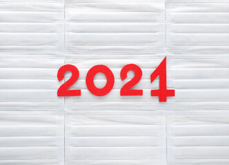 Red felt year number 2021 on light blue medical masks background. One in the form of a syringe needle. Vaccination against coronavirus success results in this year. Review of efficiency.