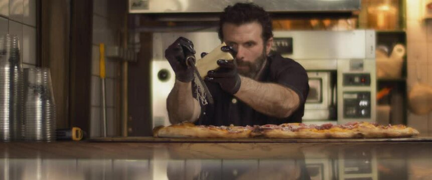Italian chef grating parmesan cheese over special al taglio pizza with roast beef topping. Medium shot, slow motion.