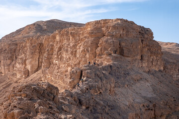 Obraz premium A group of hikers going along steep ridge. Hard and dangerous hiking trail. Extreme climbing and adrenaline. Amazing mountain landscape in Makhtesh Ramon, Negev desert, Israel 