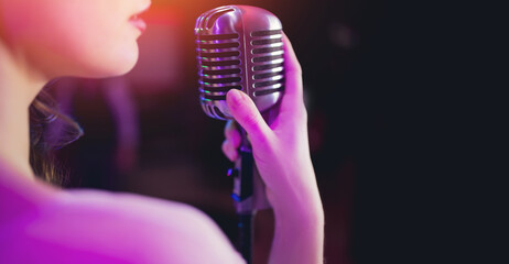 Woman vocalist holds in hand old retro microphone on dark background banner