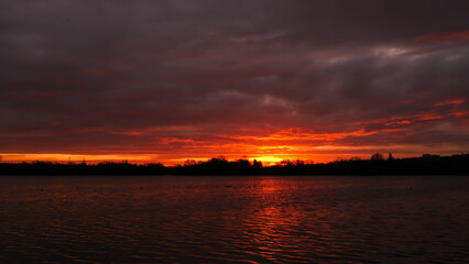 Amazing sunrise or sunset over a lake. Dramatic red sky on the horizon with water on the foreground. 